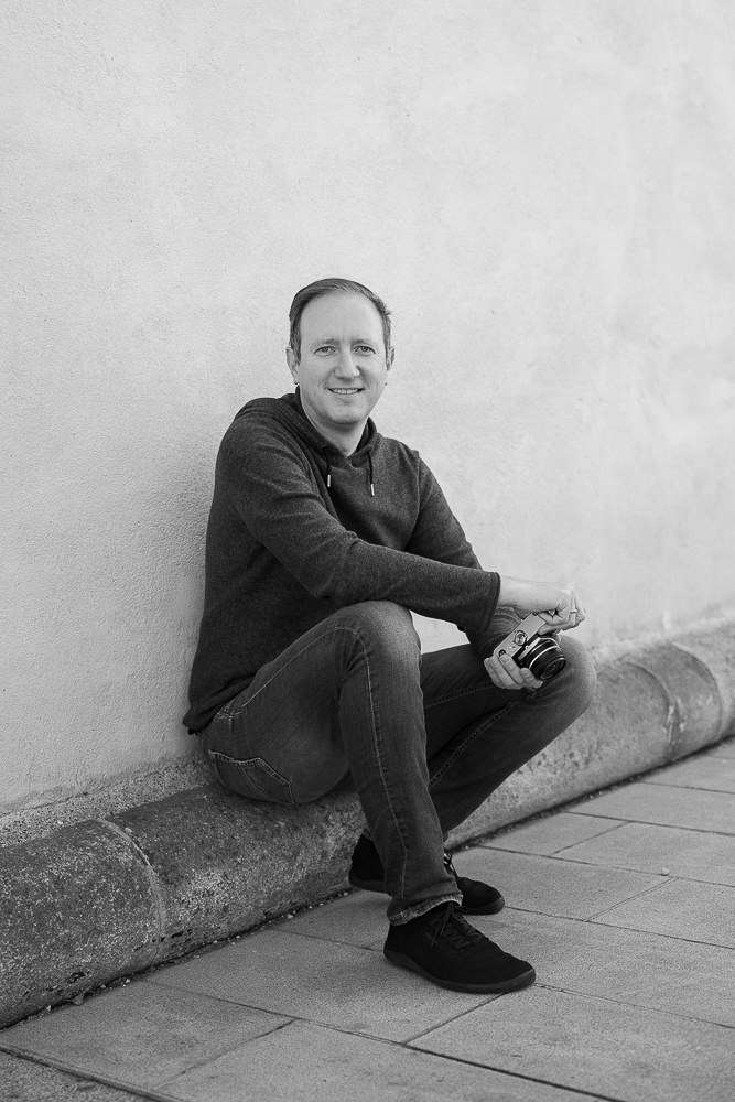Michael Keplinger, wedding photographer from Linz, Austria, sitting against a wall with his camera, black and white portrait